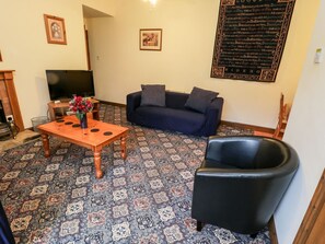Ein Wohnzimmer mit einer Couch, einem Couchtisch, einem Fernseher und einem gemusterten Teppich.