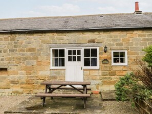 Ein Steinhäuschen mit einer weißen Tür, einem kleinen Fenster und einem Schild mit der Aufschrift 'Forge Cottage'.