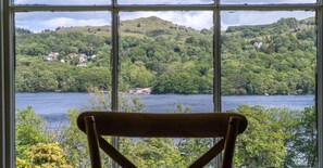 Blick durch ein Fenster, im Vordergrund ein Holzsessel, mit Blick auf einen See und Häuser an den Hügeln.