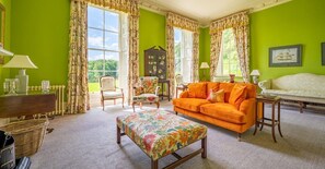 Ein Zimmer mit einer grünen Wand, einem floralen Pouf, einem orangefarbenen Sofa und einem weißen Sofa.