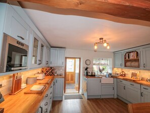 Eine Küche mit weißen Schränken, einer Holz Arbeitsplatte, einem eingebauten Backofen und einer Pendelleuchte.