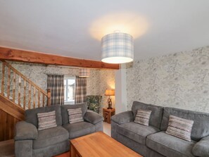Ein Wohnzimmer mit zwei grauen Sofas, einem Holztisch, einer karierten Lampe und einer Treppe.