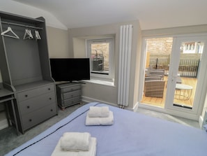 Une chambre à coucher comprenant un lit, une télévision, une armoire et un balcon aménagé avec du mobilier d’extérieur.