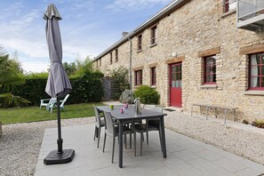 An outdoor patio with a table and chairs, a covered umbrella, and a stone building with red-framed windows.