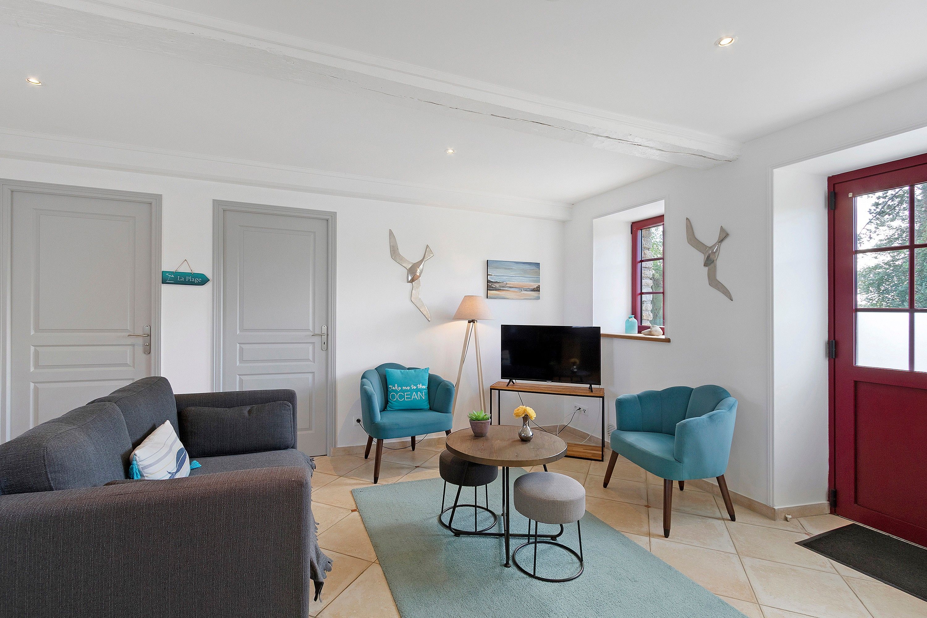 Ein Wohnzimmer mit einer Couch, Sesseln, einem Couchtisch, einem Fernseher und einer roten Tür.