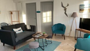 A living room with a sofa, armchair, ottoman, coffee table, and a television. - Baie des Veys Cottage near Utah Beach (Brucheville)