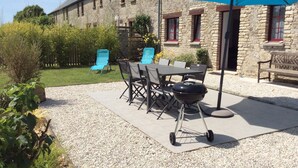 An outdoor patio with a table, chairs, a grill, and a stone building in the background. - Baie des Veys Cottage near Utah Beach (Brucheville)