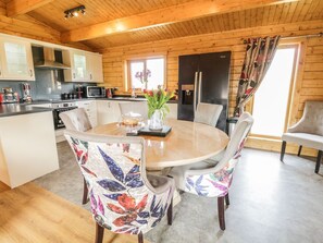 En stuga med träinredning, som innehåller ett kök, en matplats och ett stort fönster.