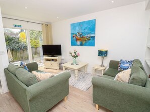 Ein Wohnzimmer mit grünen Sofas, einem Flachbildfernseher, einem Gemälde eines Bootes und einem kleinen Tisch mit einer Vase.