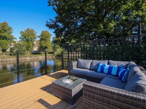 A deck with a sofa and a coffee table, overlooking a body of water and trees. - Riverside Cottage, Shrewsbury (Shrewsbury)
