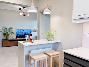 Una cocina moderna con encimera blanca, dos taburetes de madera, una botella de vino y una planta en maceta.