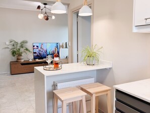 Una cocina moderna con encimera blanca, taburetes de madera, una botella de vino y una planta en maceta.