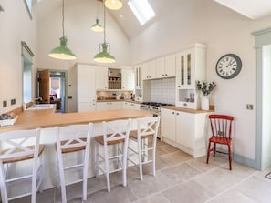 A kitchen with white cabinets, a wooden island, and hanging green pendant lights.