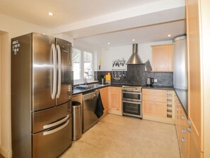 A modern kitchen with stainless steel appliances, wooden cabinets, and a tiled backsplash. - Estuary View, Newton Ferrers (Plymouth)