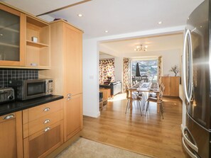 A kitchen with wooden cabinets, a stainless steel refrigerator, and a dining area with a table and chairs. - Estuary View, Newton Ferrers (Plymouth)