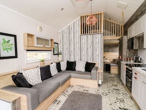 A modern living room with a sectional sofa, a kitchen area, and a staircase leading to an upper level.