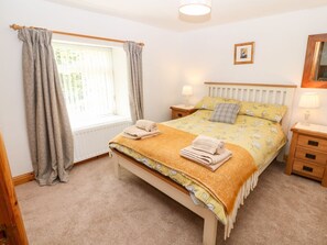 A bedroom with a bed, two bedside tables, a window with curtains, a radiator, and a wall-mounted mirror. - Cefn Werthyd Farmhouse Retreat (Caernarfon)