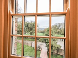 A window with a view of a brick wall, a grassy area, and a stone pathway.