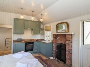 Eine kompakte Küche mit Kamin aus Backstein, ein Essbereich mit gedecktem Tisch und ein Schlafzimmer mit Bett.