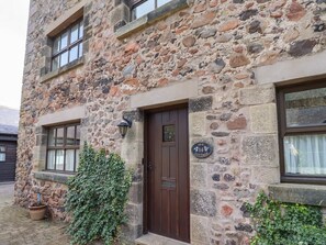 A stone building with a brown door, windows, and a sign reading 'Ivy Cottage.' - Charming Ivy Cottage Retreat (Wooler)