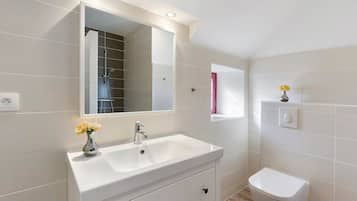 A modern bathroom with a white sink, mirror, and toilet.