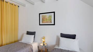 A room with two beds, a small table with a lamp, and a framed picture on the wall.