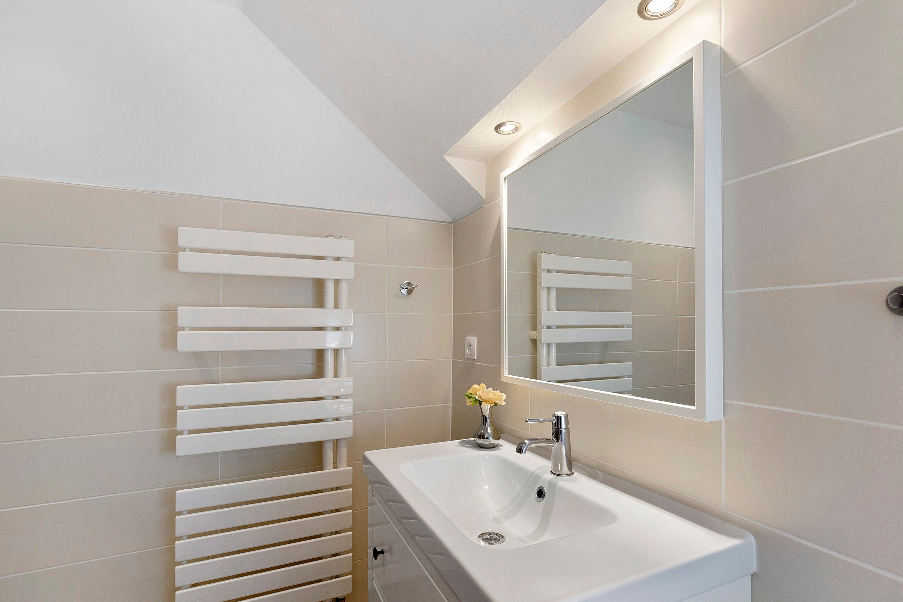 Un baño moderno con un lavamanos blanco, un espejo y un perchero para toallas.