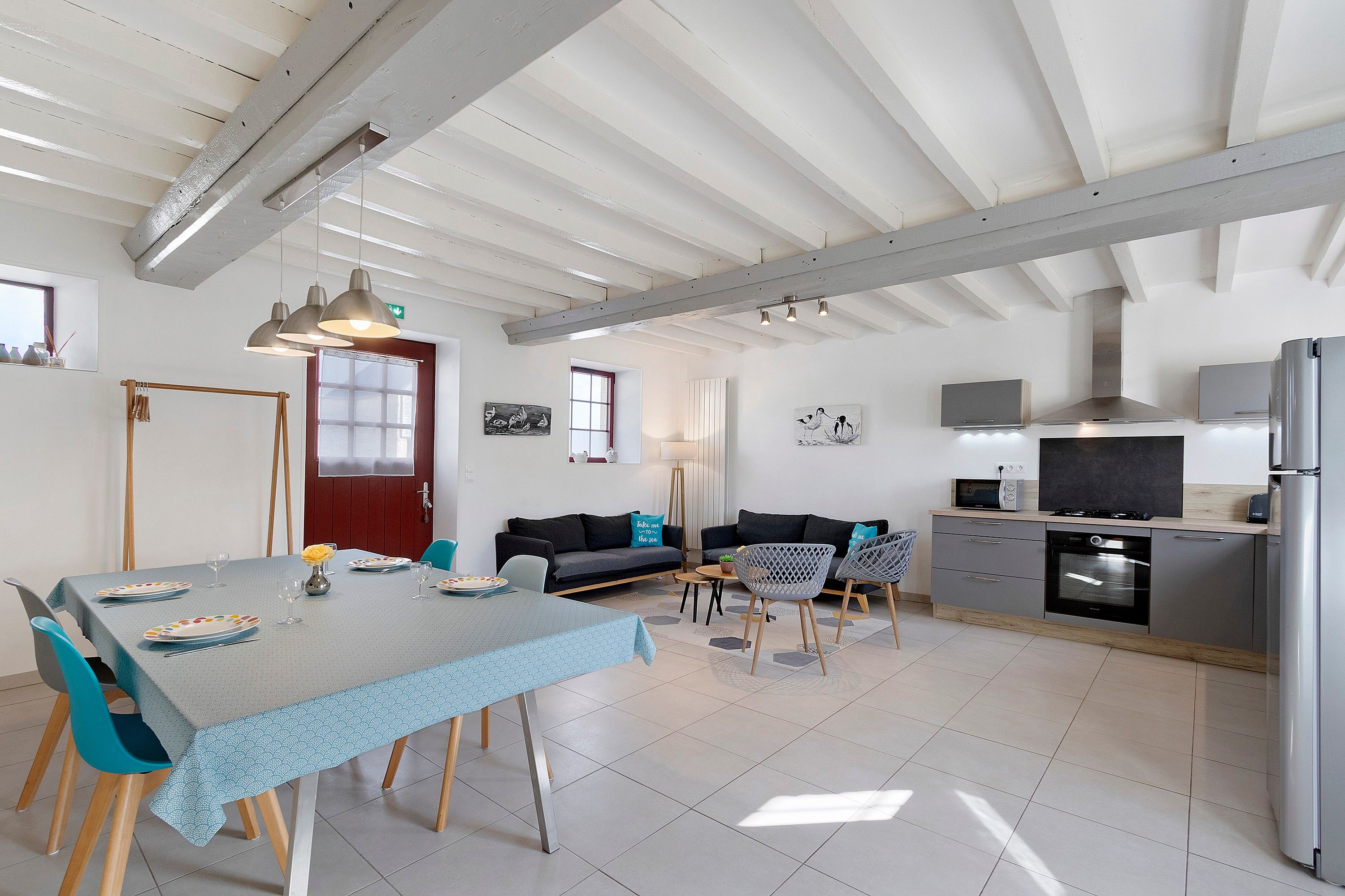 Une cuisine moderne avec un coin repas, comprenant une table dressée pour quatre personnes, un canapé et un îlot de cuisine équipé d’appareils électroménagers.
