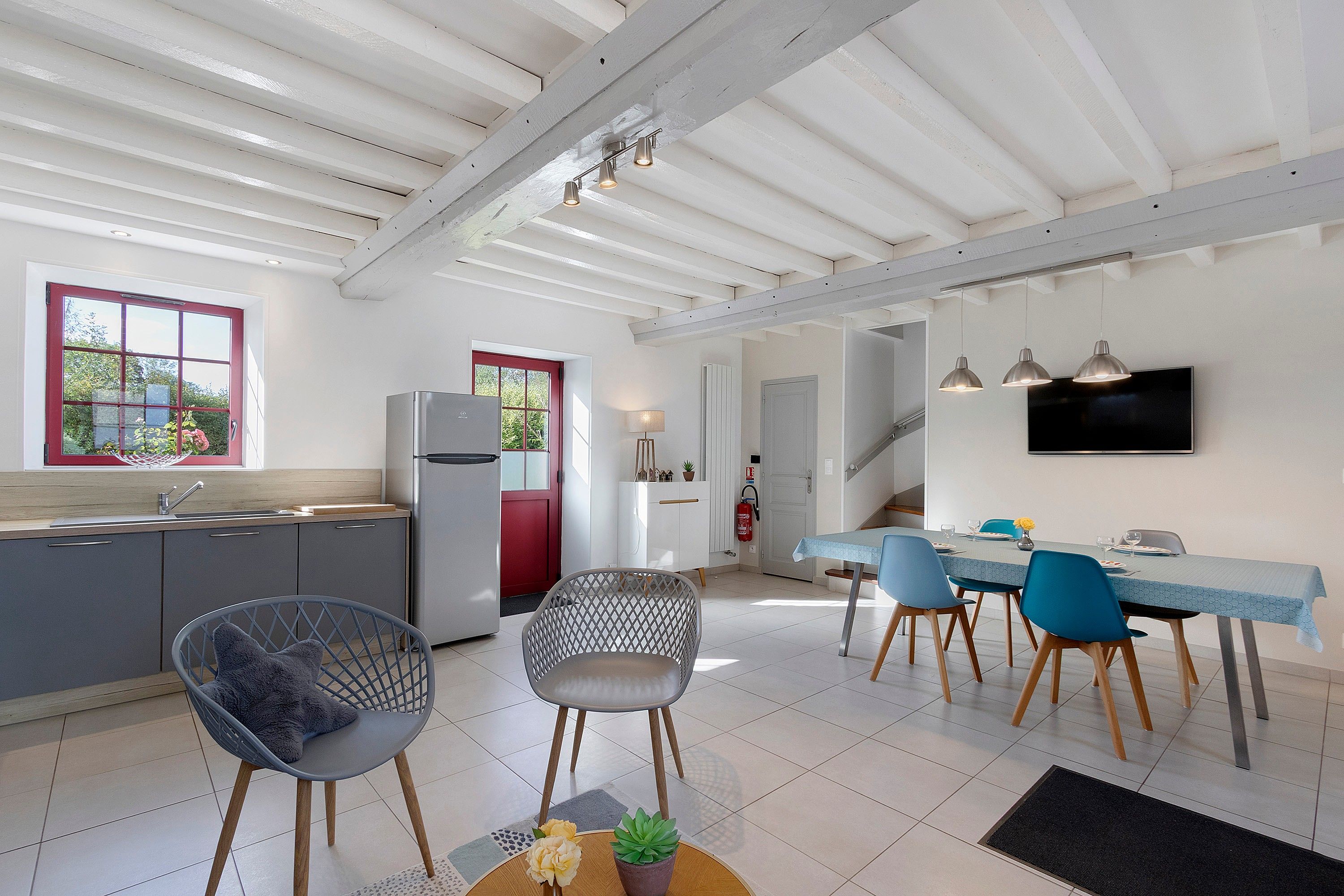 Una cocina moderna con refrigerador, un comedor con sillas y una mesa, y una escalera que lleva a otro nivel.