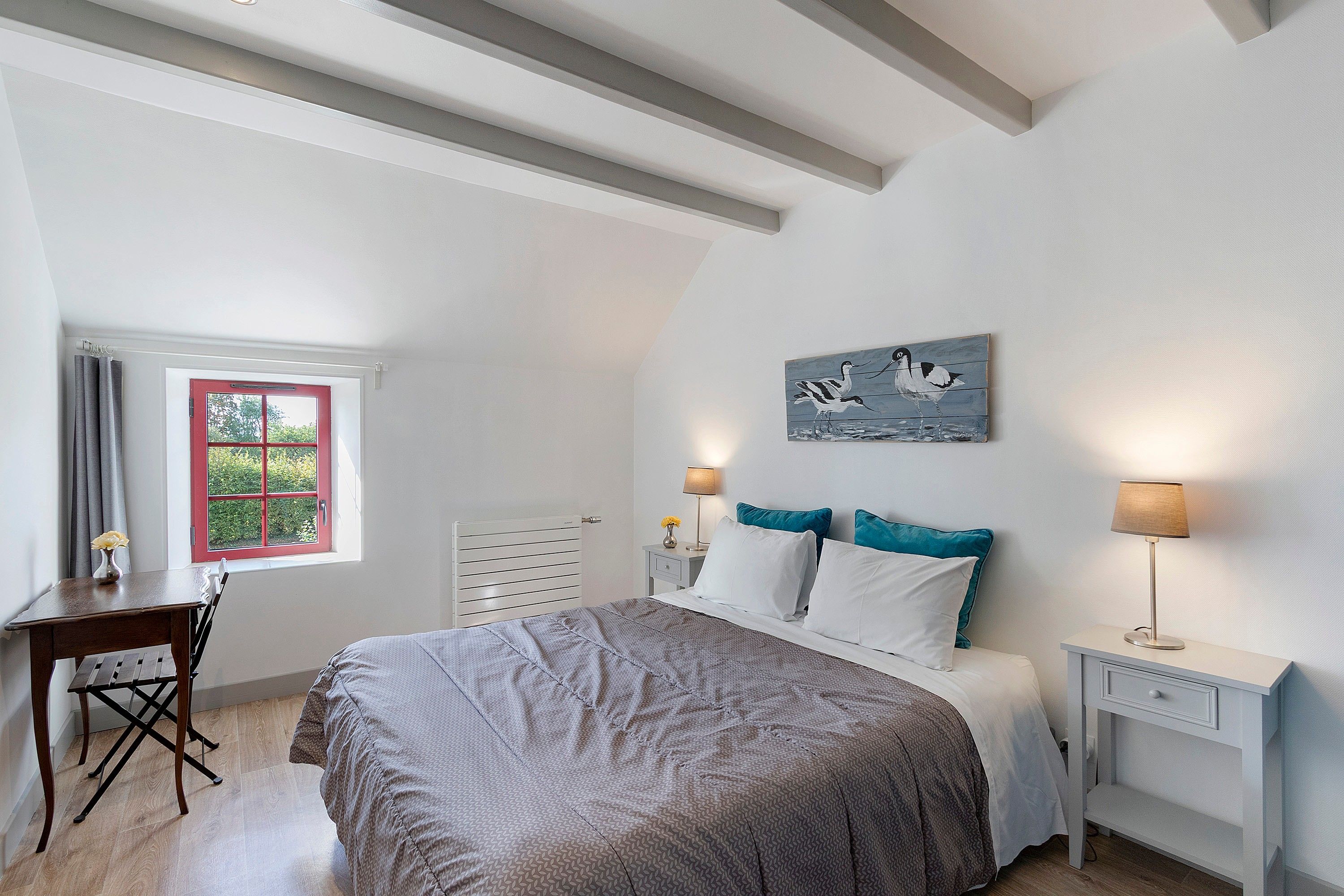 Een slaapkamer met een bed, nachtkastjes, een bureau en een raam met gordijnen.