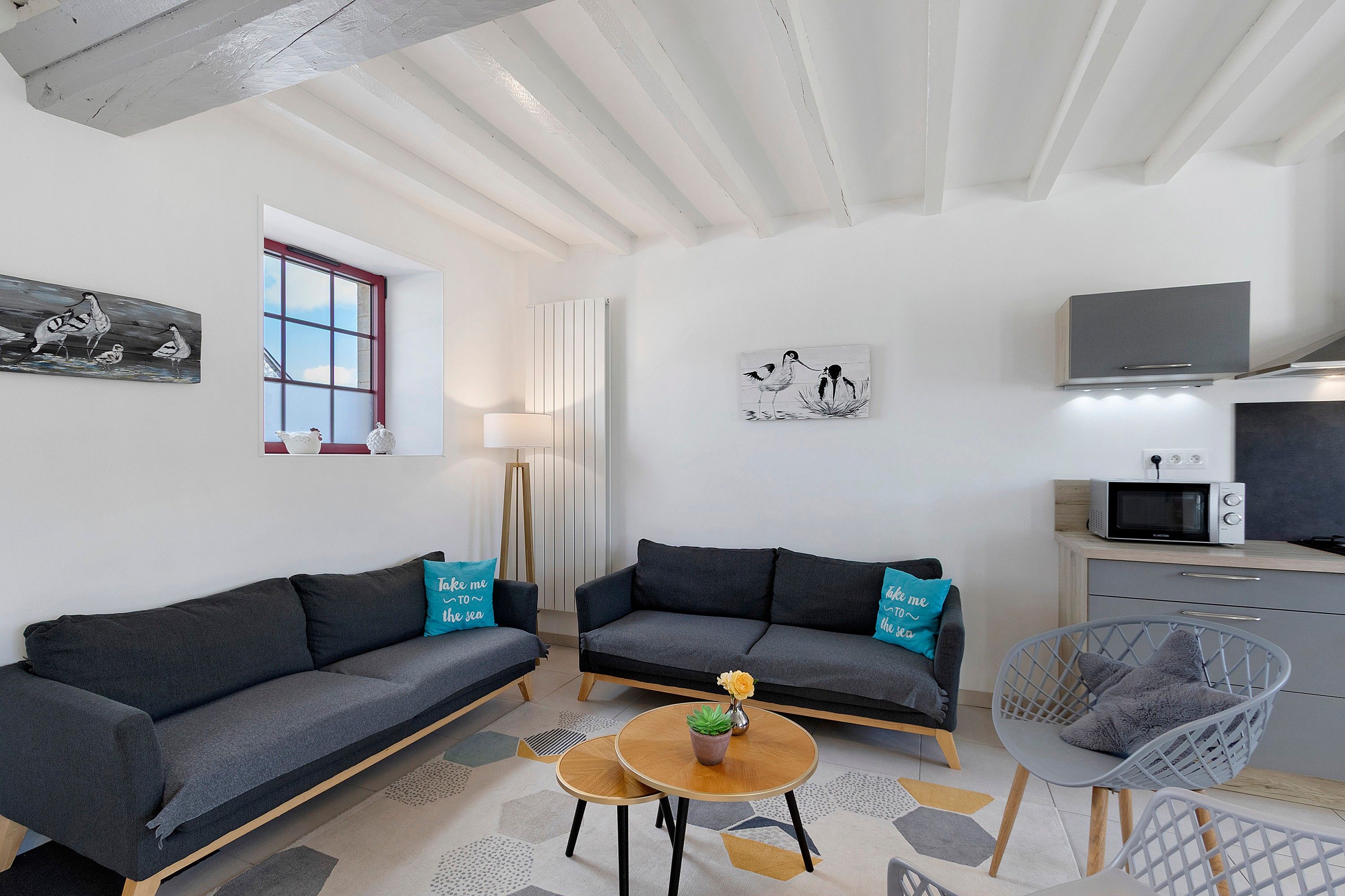 A modern living room with two sofas, a small table, a chair, and a kitchen area with a microwave.