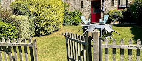 A stone building with a red door, a fenced garden, and outdoor seating.