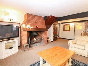 A living room with a brick fireplace, a television, a wooden table, and a white sofa. - Phloxhaven: A Charming Retreat in Reedham (Norwich)