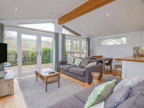 A modern living room with a sofa, coffee table, and a television. There is a sliding glass door leading to an outdoor area.