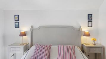 Un lit bien fait, agrémenté d’oreillers à rayures, deux tables de chevet avec des lampes et des tableaux encadrés accrochés aux murs.