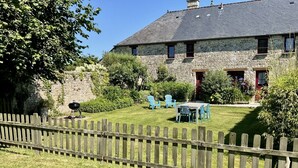 Un bâtiment en pierre avec une cour verdoyante, une clôture en bois et des sièges à l’extérieur.