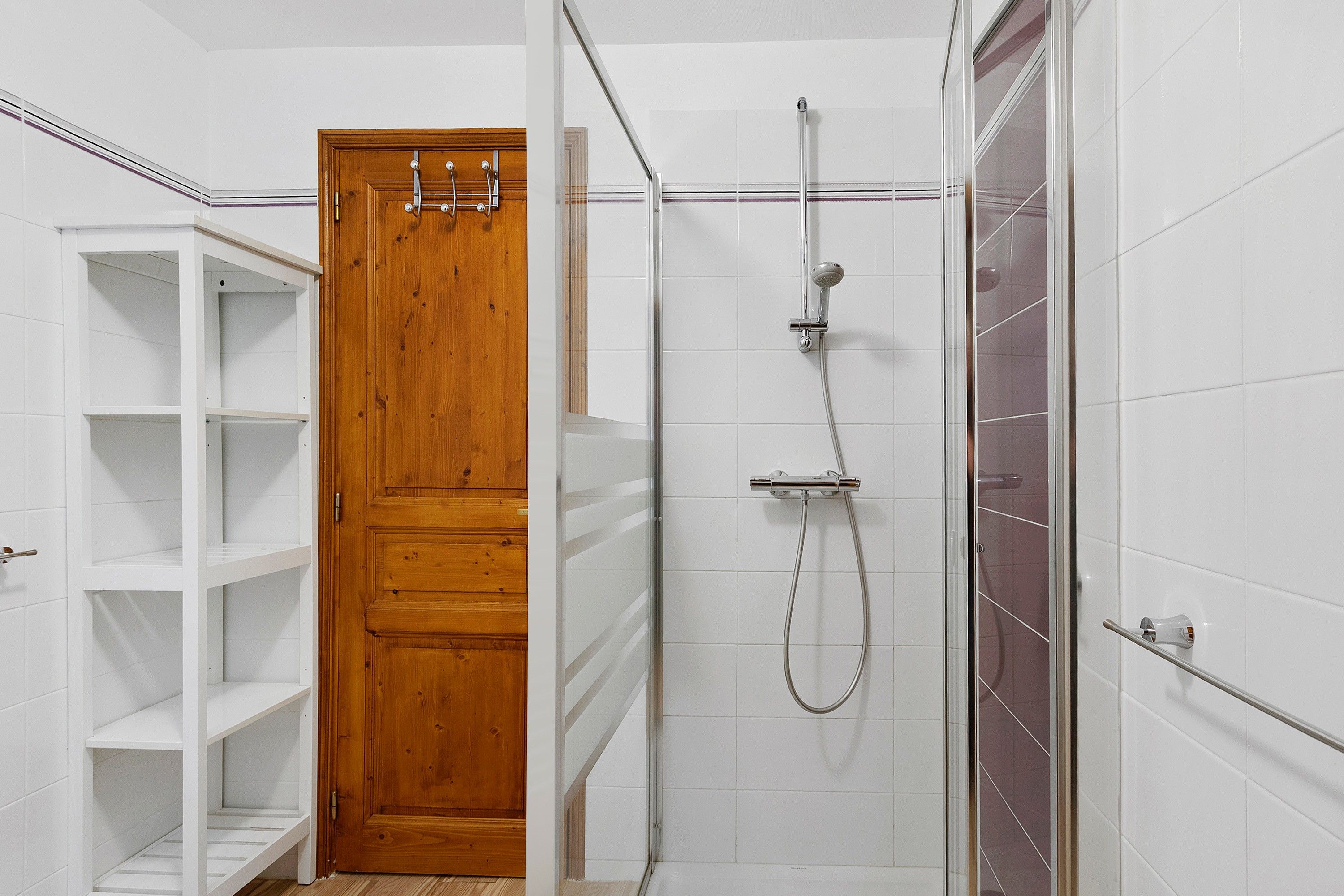 Ein Badezimmer mit Dusche, einer Holztür und weiß gefliesten Wänden.
