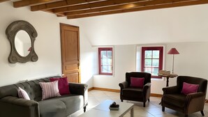 Un salon avec un canapé, des fauteuils, une table basse, une porte en bois et des fenêtres.