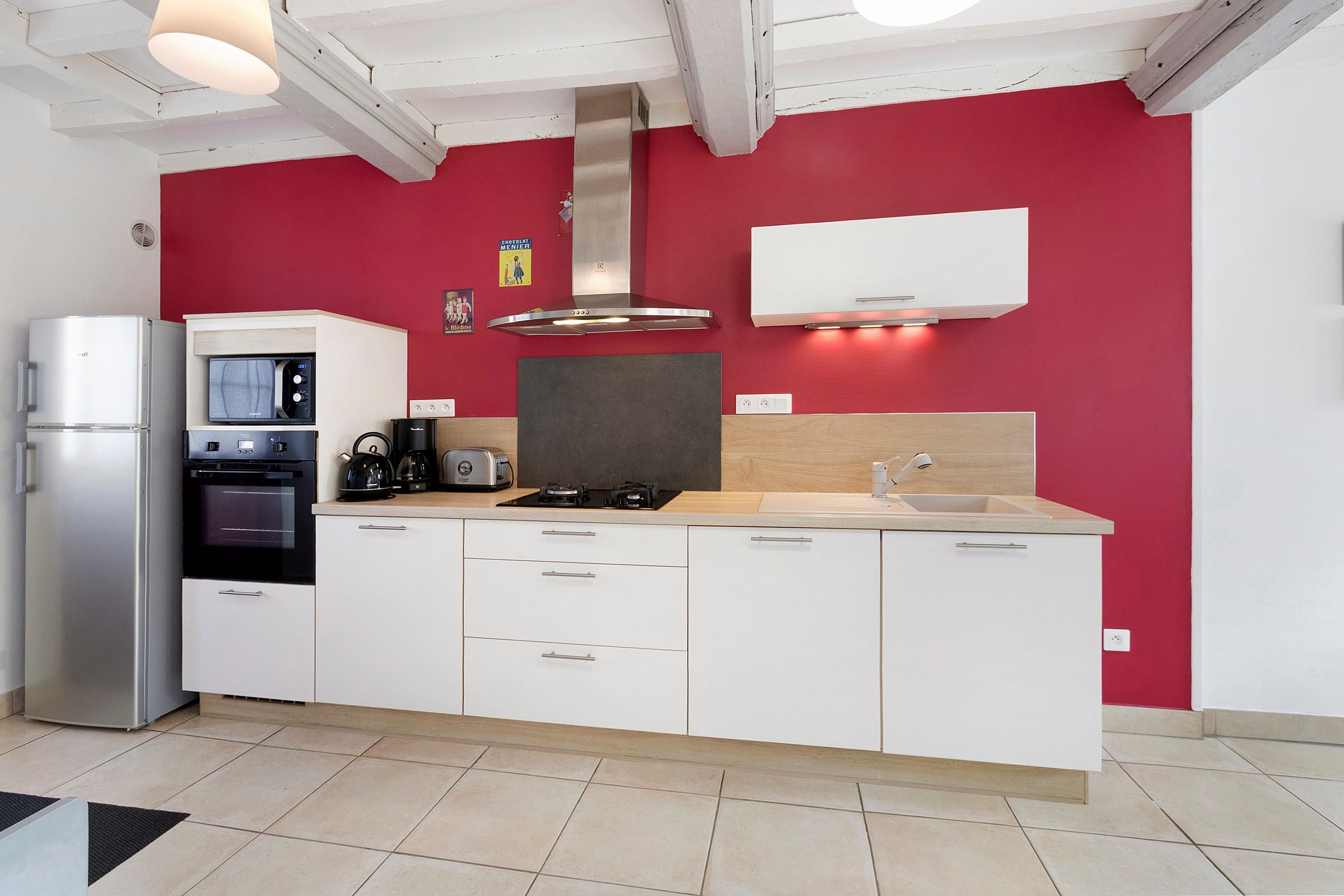 A modern kitchen with white cabinets, a red accent wall, a built-in oven, a microwave, a gas stove, and a sink.