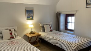 Une chambre avec deux lits, une table de chevet avec une lampe, une fenêtre avec des rideaux et un tableau accroché au mur.