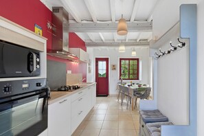 Eine moderne Küche mit Einbauherd, einer roten Wand und einem Essbereich mit Tisch und Stühlen.