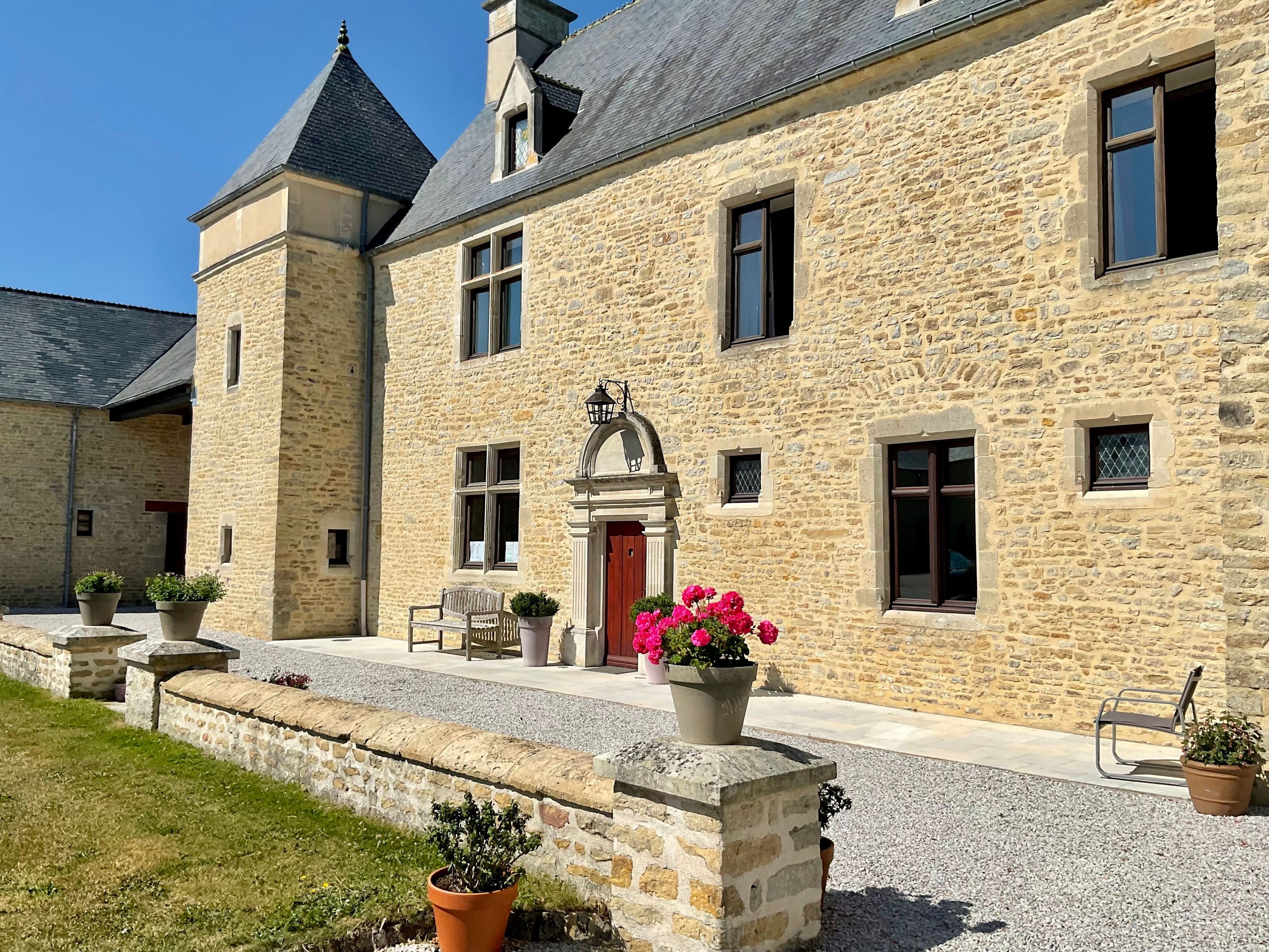 A stone building with a red door, multiple windows, and a small balcony with potted plants.