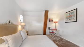 Een slaapkamer met een bed, nachtkastje, lamp, houten balk, stoel, tafel en een schilderij aan de muur.