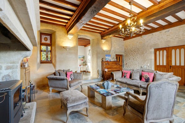 A cozy living room with a fireplace, wooden beams, and a stone wall.