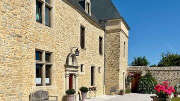 Un bâtiment en pierre avec une allée de gravier, un banc et des plantes en pot.
