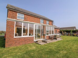 A two-story brick house with a large glass conservatory, a patio with outdoor furniture, and a well-maintained lawn. - CADWAGAN, hot tub, WiFi, near Aberporth (Cardigan)