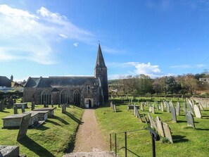 Una iglesia con una aguja alta, un cementerio con lápidas y un cielo despejado.