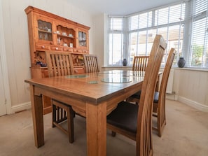 Un comedor con una mesa y sillas de madera, un aparador de madera con puertas de cristal, y una ventana con persianas.