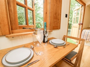 Une table de salle à manger en bois, mise avec des assiettes, des couverts et un verre à vin, avec une fenêtre et des meubles en bois en arrière-plan.