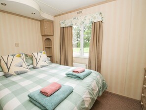 Ein Schlafzimmer mit karierter Bettdecke, zwei Kissen, einem Fenster mit Vorhängen und einem Holzkasten.